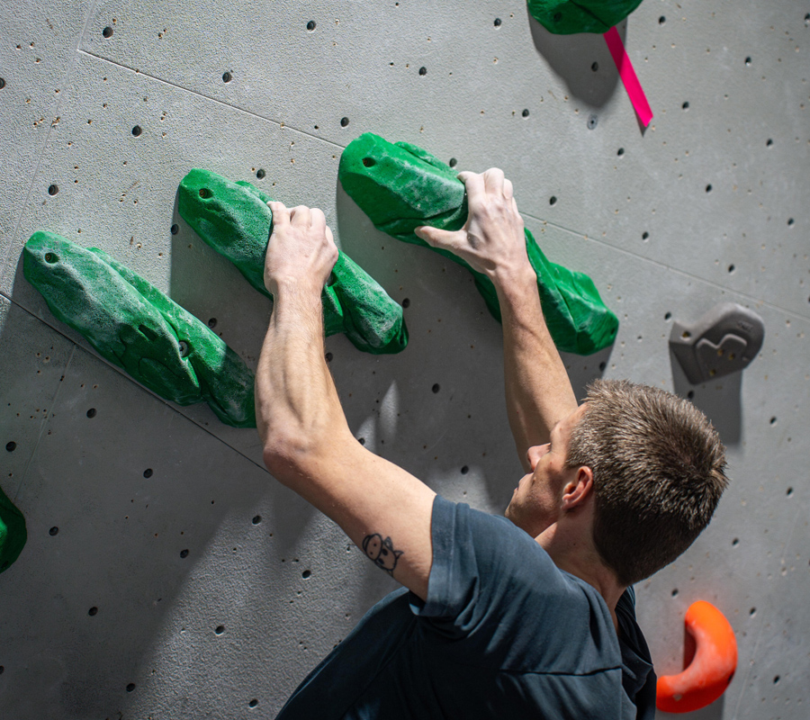 A man holds onto the top of 3 almost horizontal holds as he progresses up the wall.